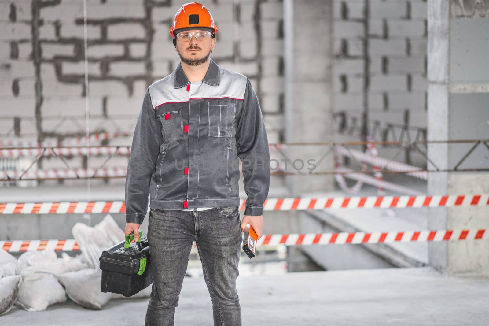 Construction workman ready for renovation work. Builder in uniform carrying toolbox at construction site, copy space by Rom4ek
