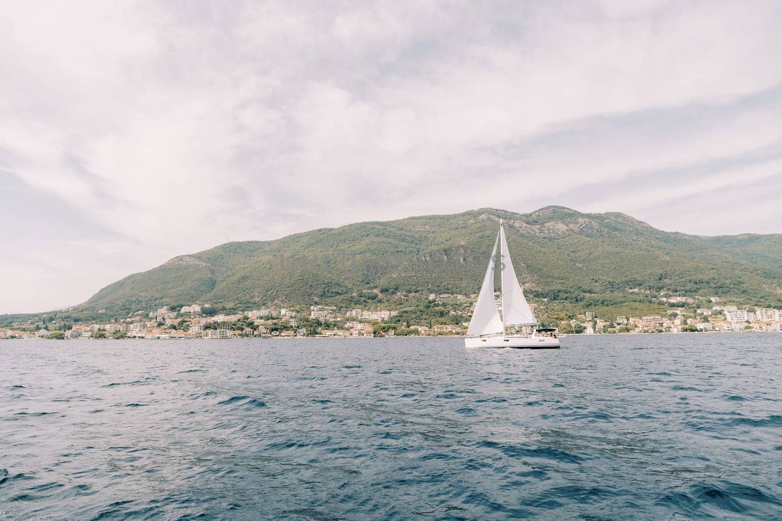 White sailboat sails on the sea along the mountainous coast. High quality photo