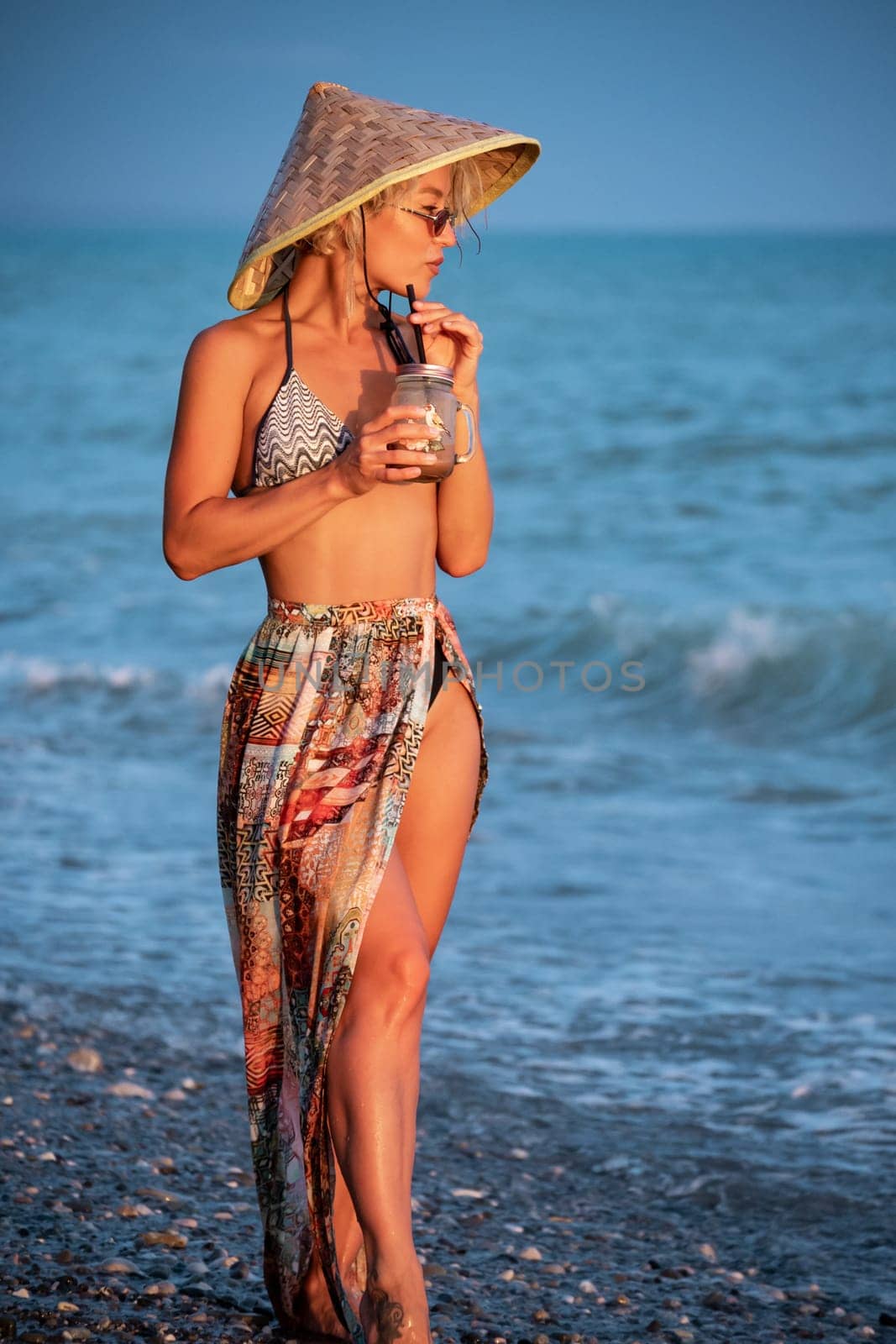 beautiful girl with a smoothie by the sea in straw Asian triangular hat