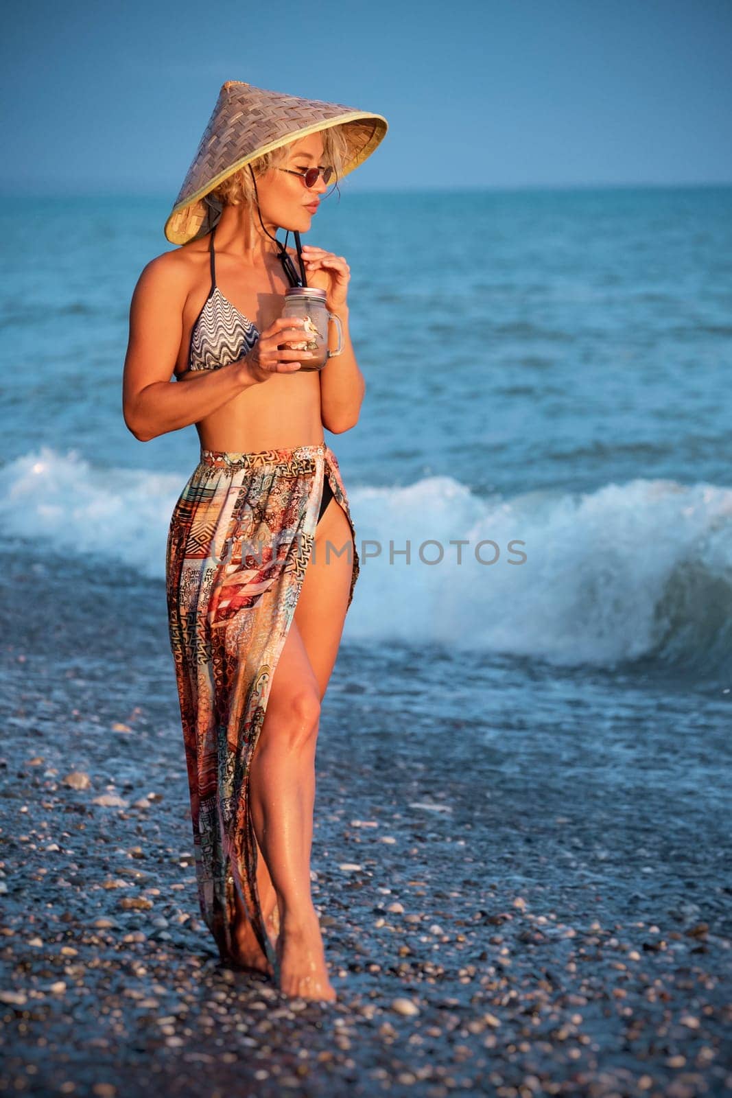 beautiful girl with a smoothie by the sea in a straw Asian triangular hat by Rotozey