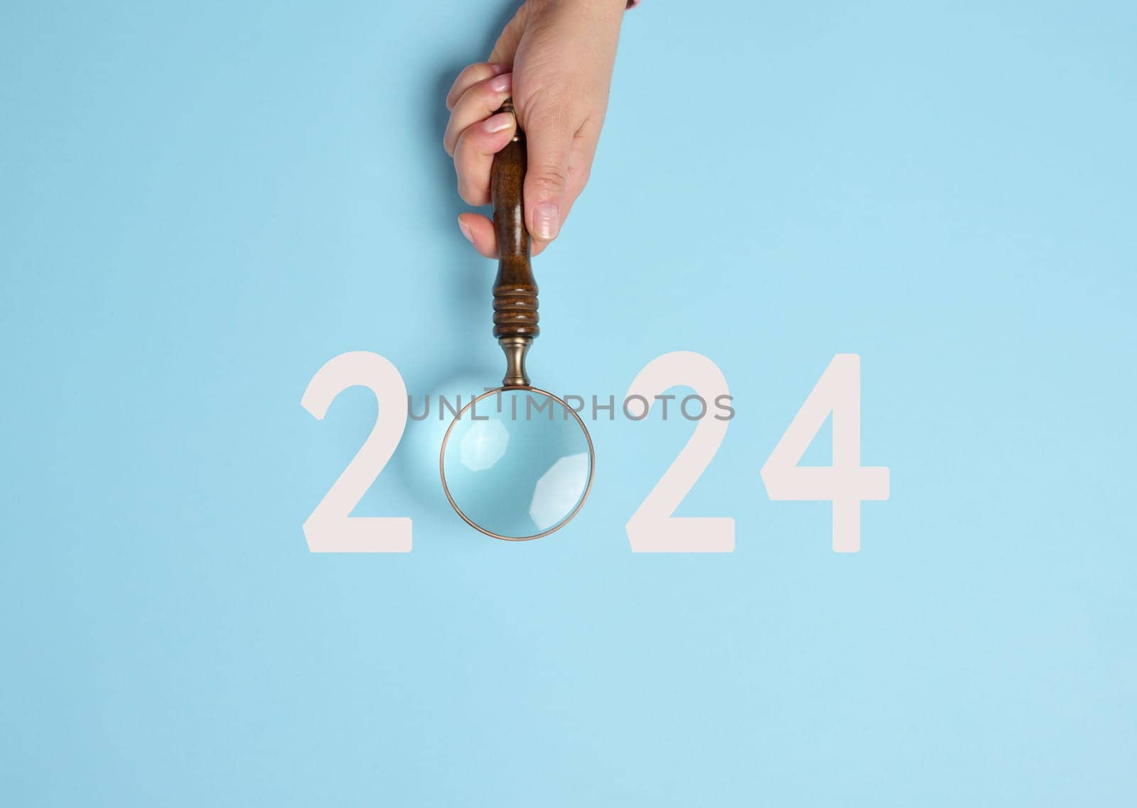 A female hand holds a magnifying glass and the inscription 2024, symbolizing the arrival of the new yea