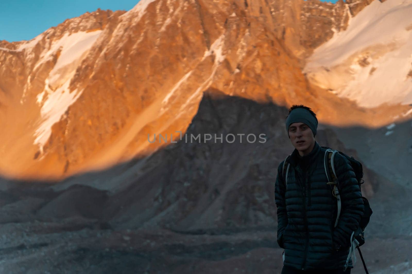 Silhouette of a young man traveling through the snow-capped mountains in spring at sunset in a picturesque area, a traveler with a backpack makes a solo trip through the national park.