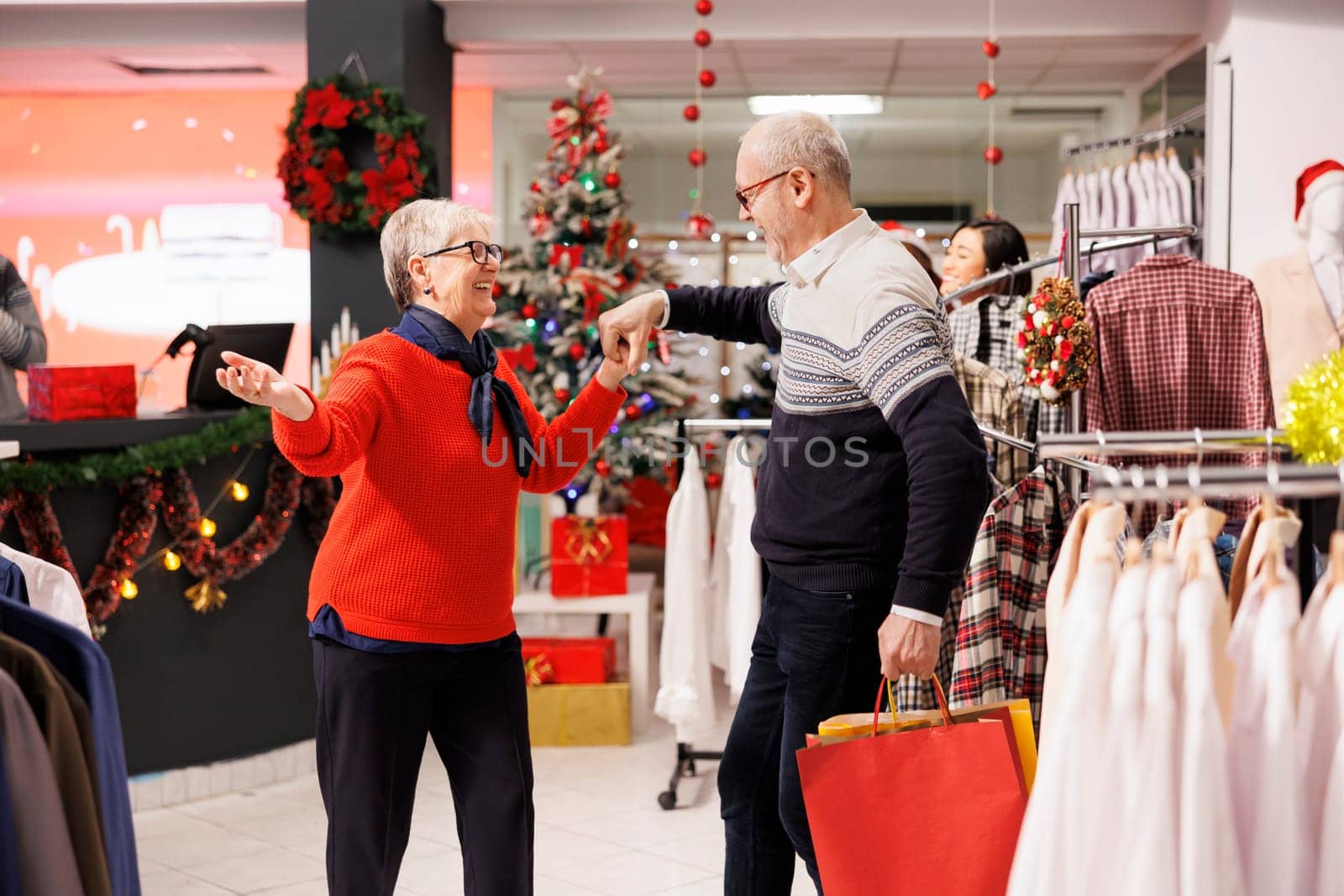Romantic couple dancing in clothing store, enjoying shopping spree for presents to buy trendy clothes on sale. Joyful senior people showing cute dance moves near hangers and racks, sincere love.