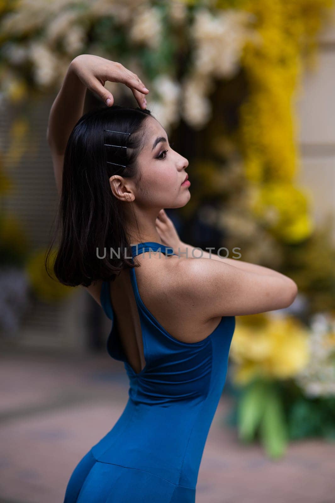 Close-up portrait of a beautiful Asian ballerina posing against the background of a building decorated with flowers. Vertical photo