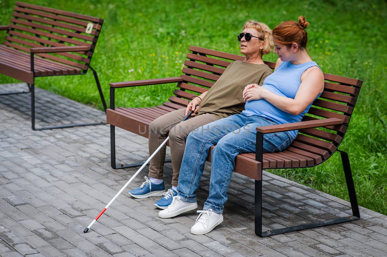 An elderly blind woman and her pregnant daughter are sitting on a bench in the park