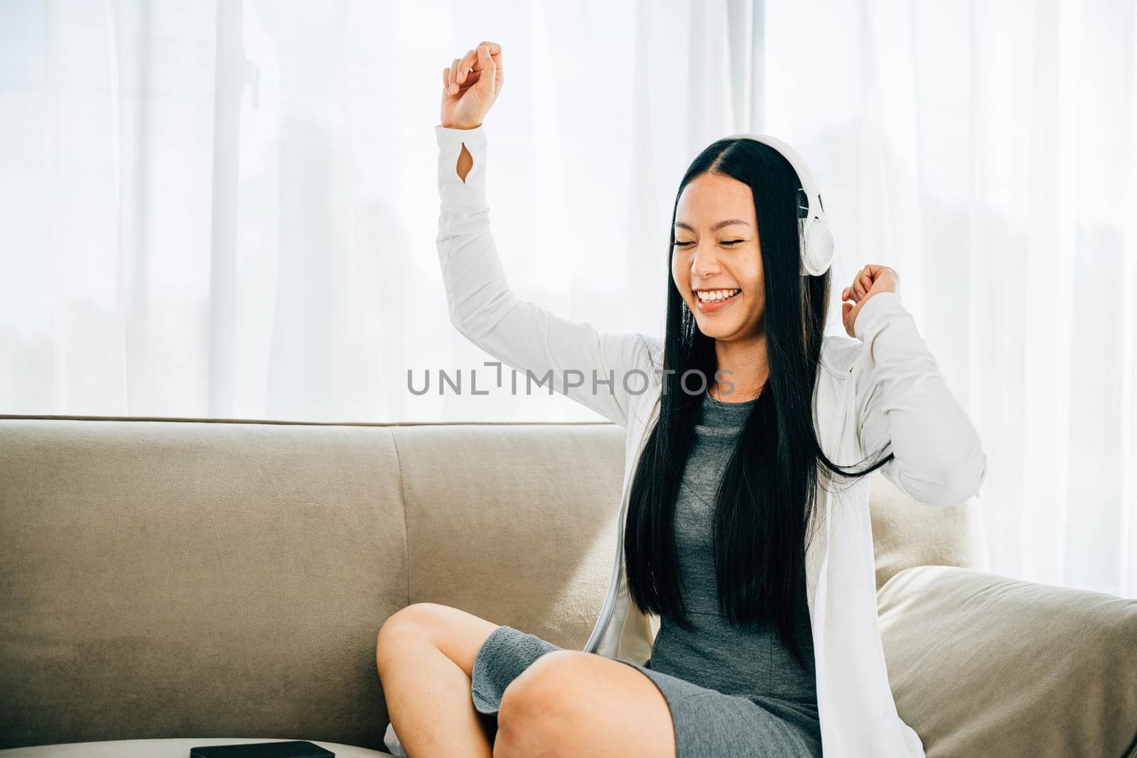 Happy woman in headphones holds phone dances and gestures on sofa by Sorapop