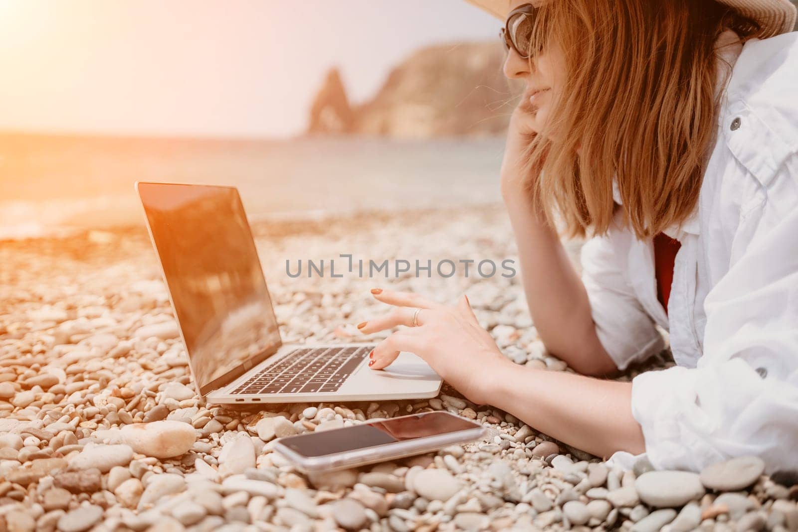 Woman sea laptop. Business woman in yellow hat working on laptop by sea. Close up on hands of pretty lady typing on computer outdoors summer day. Freelance, digital nomad, travel and holidays concept. by panophotograph
