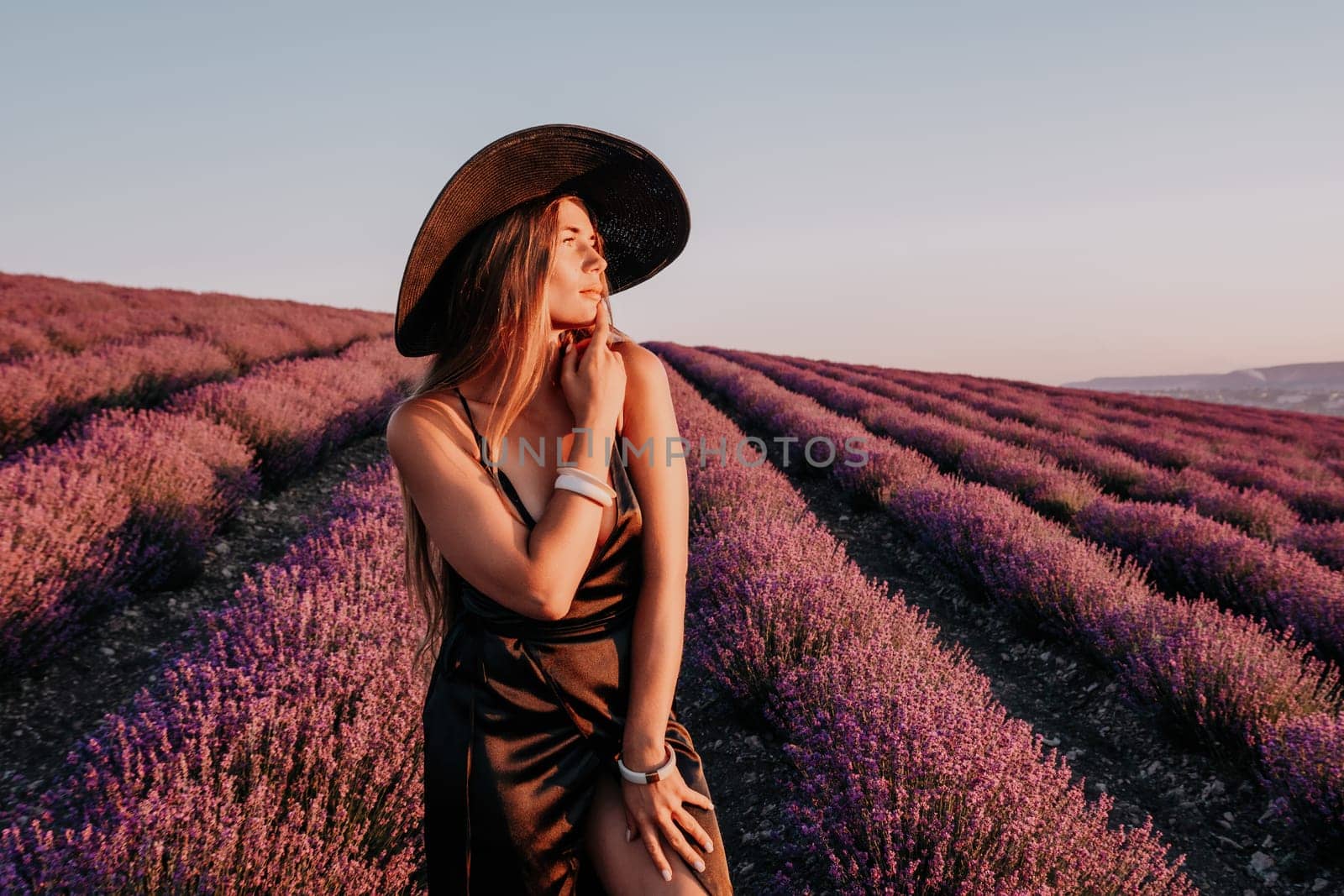 Woman lavender field. Happy carefree woman in black dress and hat with large brim walking in a lavender field during sunset. Perfect for inspirational and warm concepts in travel and wanderlust. by panophotograph