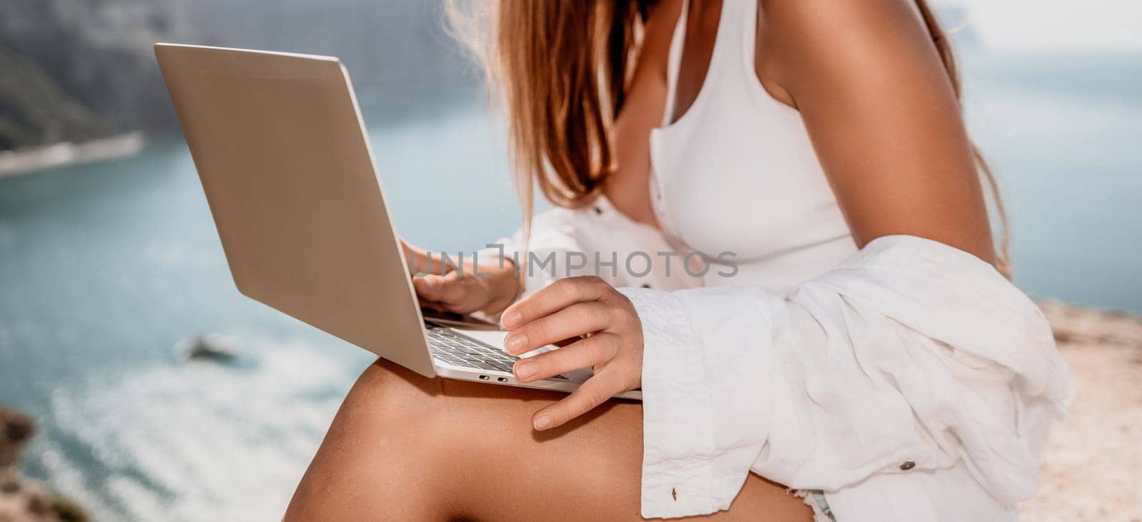 Digital nomad, Business woman working on laptop by the sea. Pretty lady typing on computer by the sea at sunset, makes a business transaction online from a distance. Freelance remote work on vacation