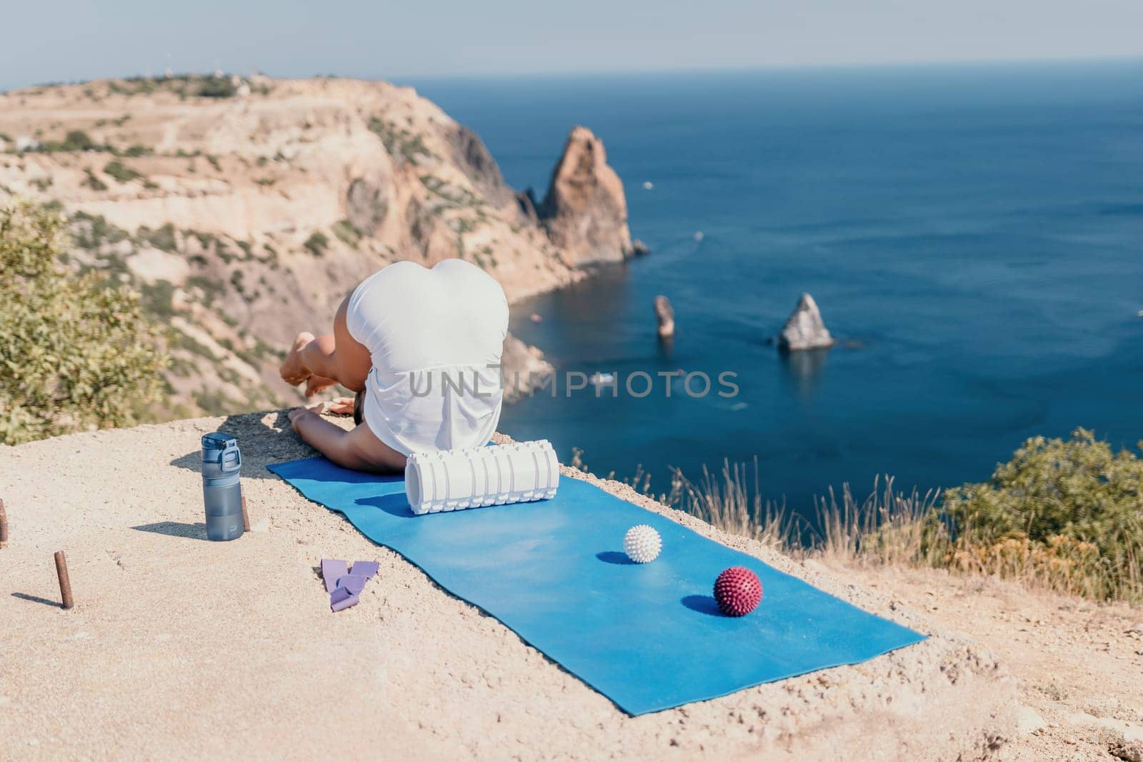 Woman sea pilates. Sporty happy middle aged woman practicing fitness on yoga mat with balls and roller near sea, smiling active female outside, enjoying healthy lifestyle, harmony and meditation. by panophotograph