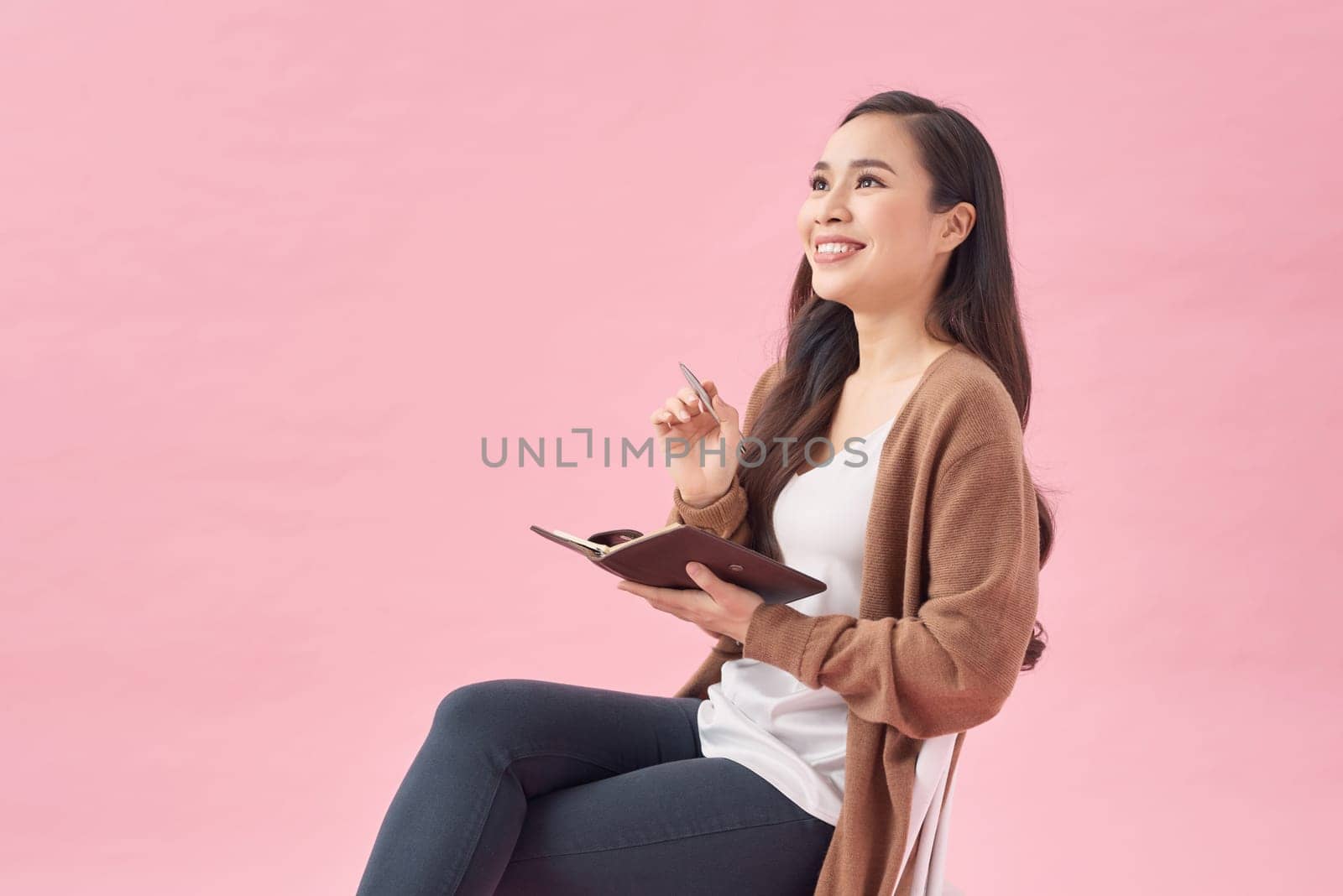 Business woman sits on a chair writes notes in her notepad on pink background by makidotvn