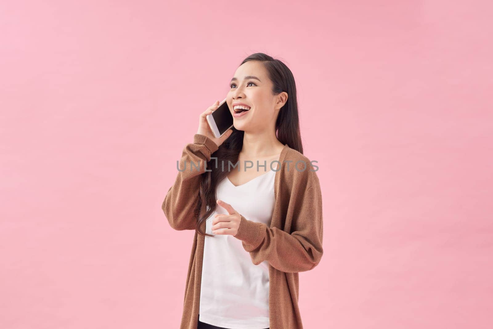 woman sitting in chair looking copyspace talking on cellphone isolated pastel pink color background by makidotvn
