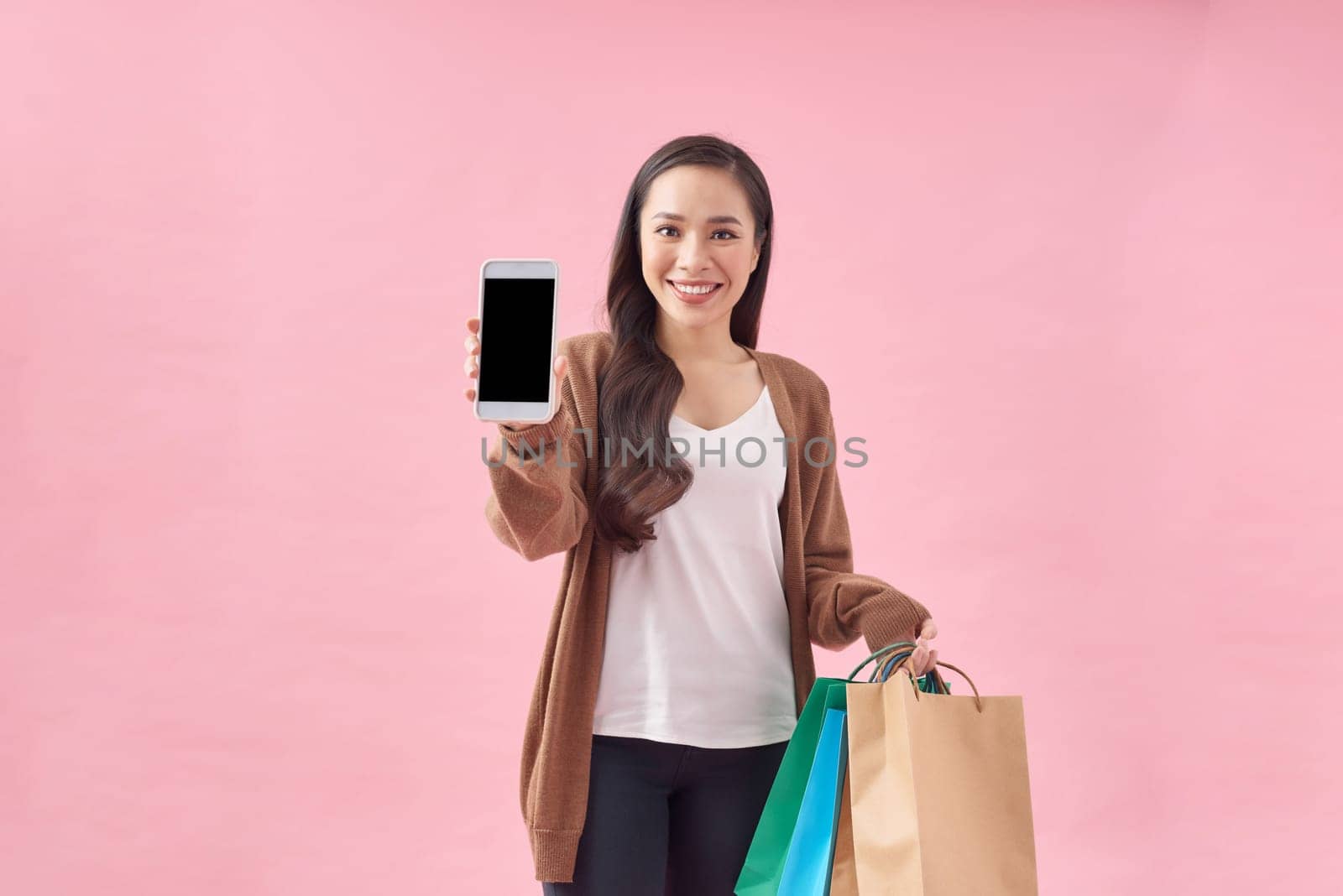 Beautiful Attractive Asian Woman holding shopping bags and showing mobile phone screen on pink