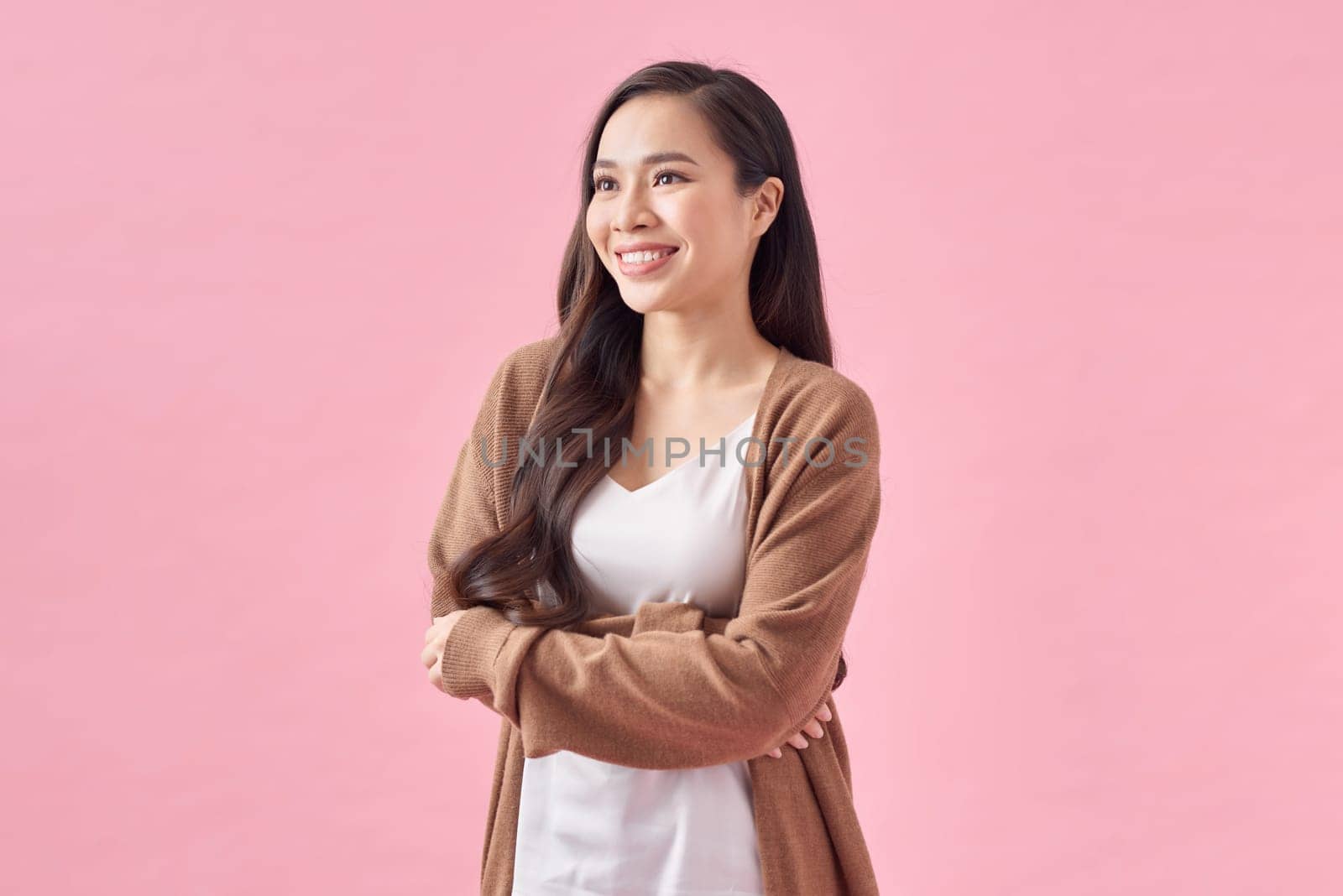 Smiling woman with arms crossed standing against pink background by makidotvn