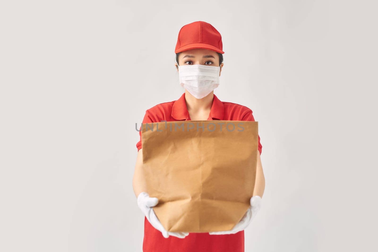 happy smiling delivery woman in red uniform with takeaway food in paper bag over white background by makidotvn