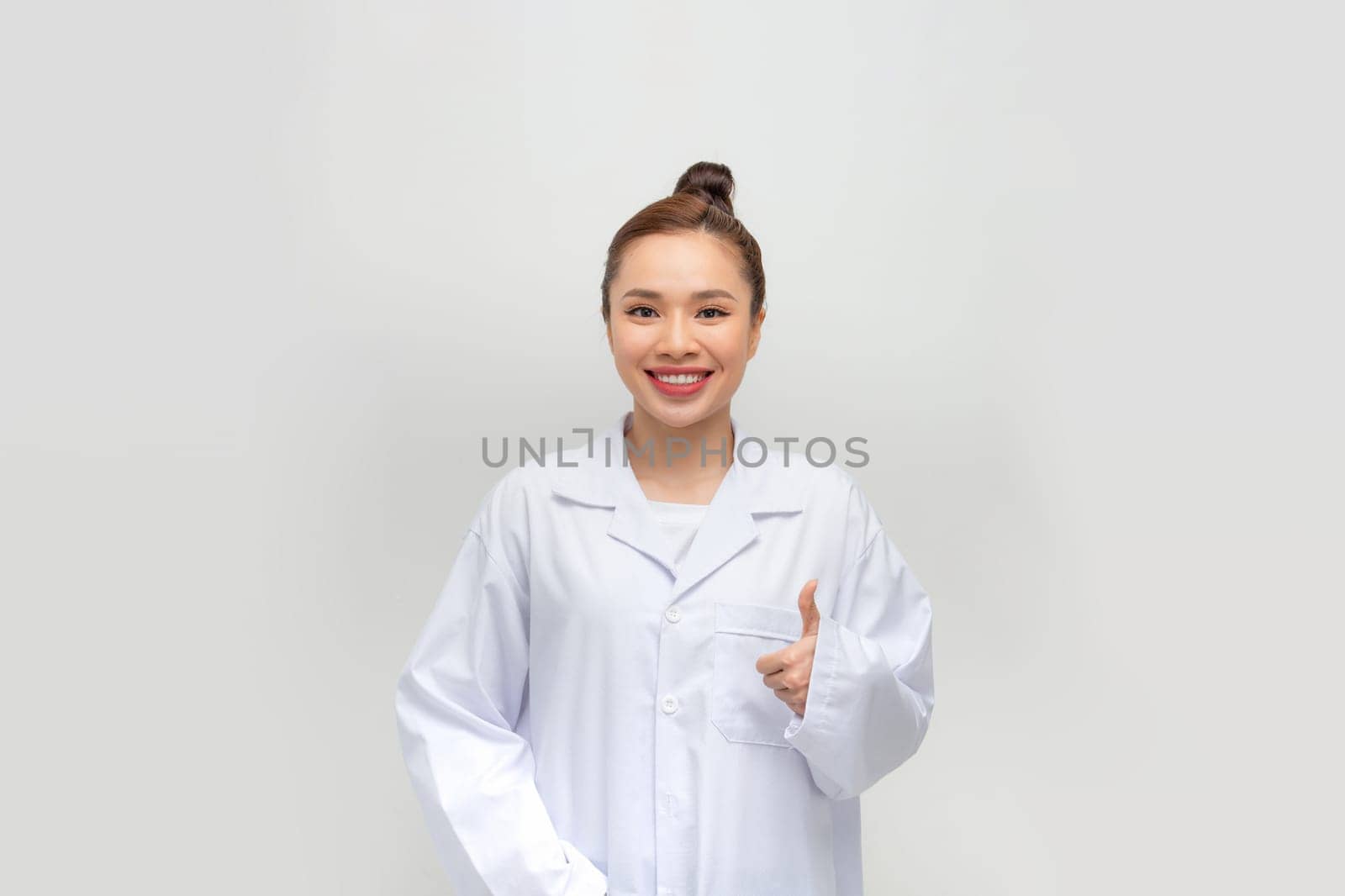 Photo of cute charming woman doc dressed white coat pointing thumb up  by makidotvn