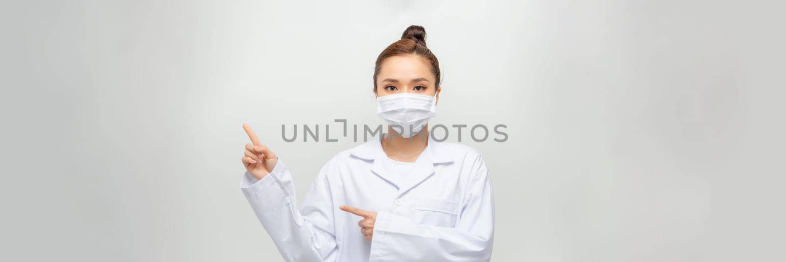 Beautiful white woman doctor lady in white coat on green background. points with her fing