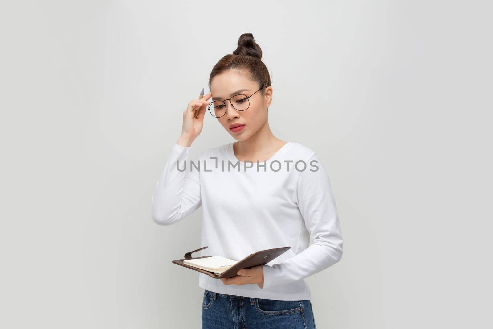 Intelligent asian lady in glasses taking notes, holding notepad and pen, standing over white by makidotvn
