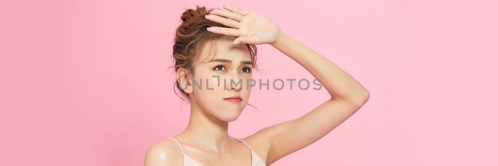 Woman covering her face from sun with her hand while standing against pink background by makidotvn