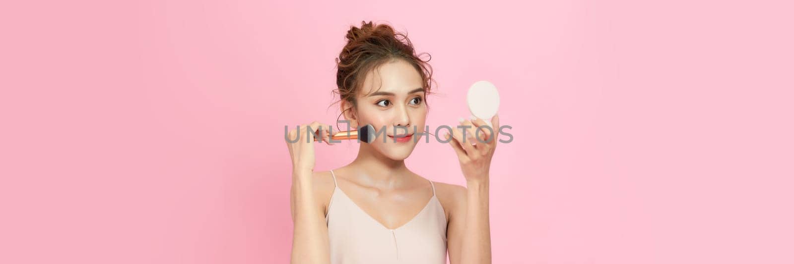 Young woman applying make-up from powder compact. by makidotvn