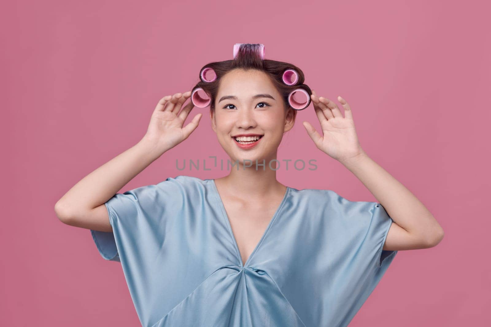 Headshot of a young woman with hair curlers over pink background