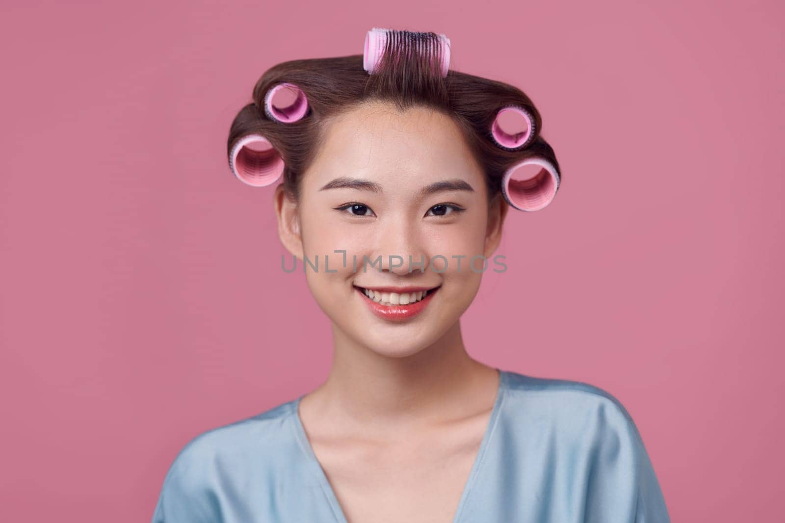 Beautiful young woman in casual dress and hair curlers on pink background
