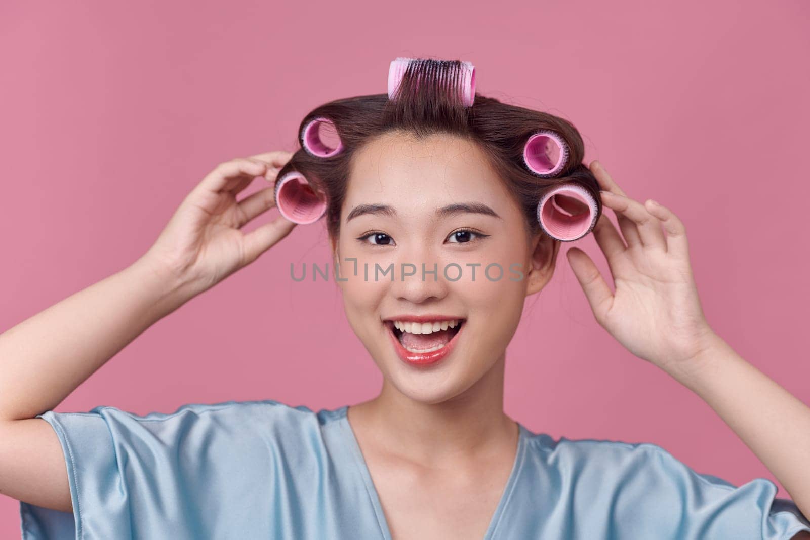 Cheerful asian girl with hair curlers rollers by hairdresser.