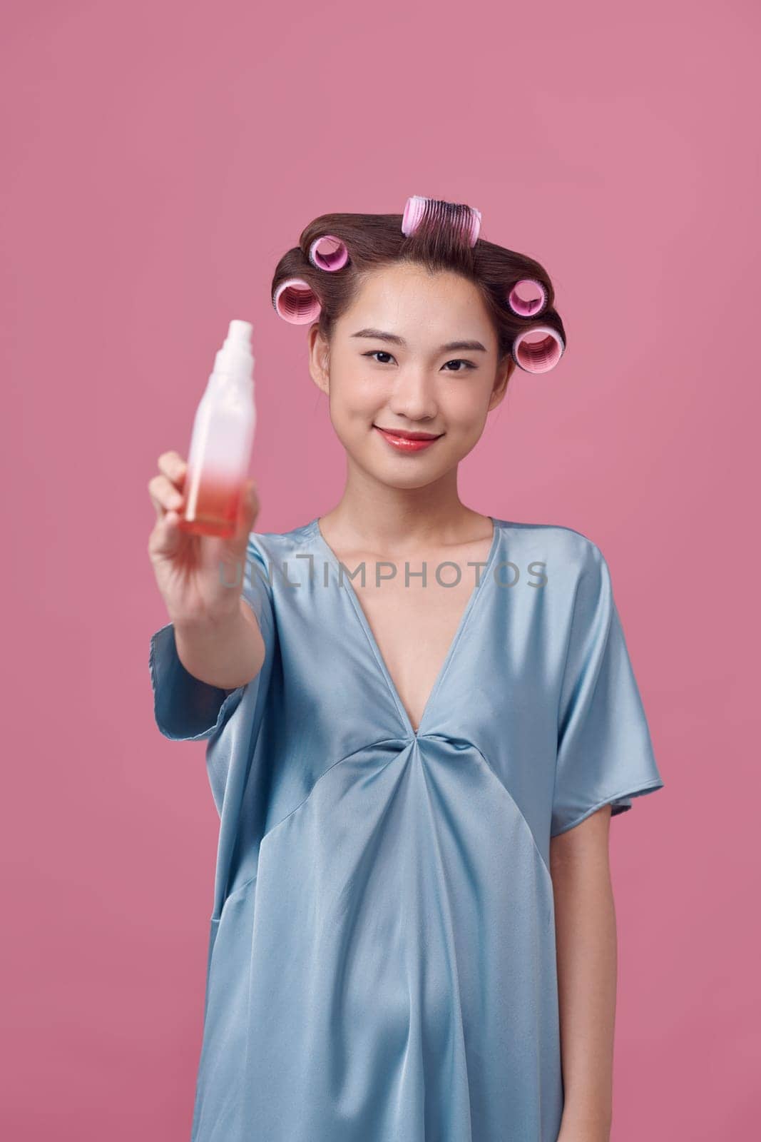 Beautiful young woman holding a bottle in her hand with curlers on her hair