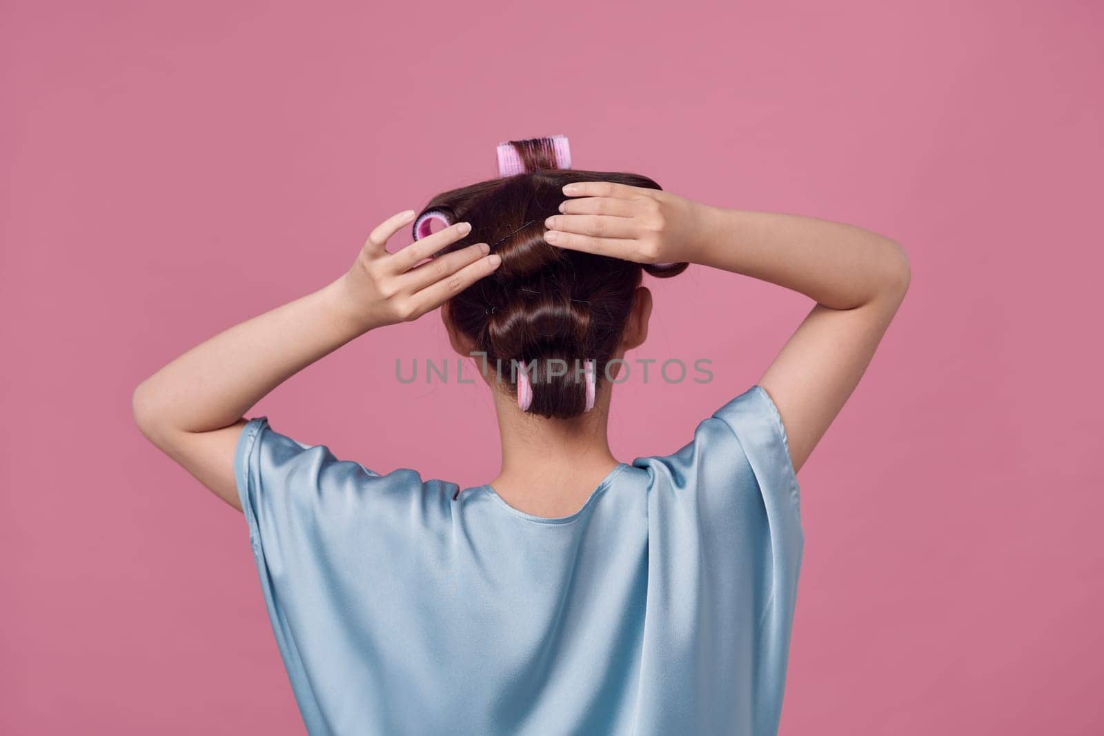 Back view of young woman with hair curlers on pink