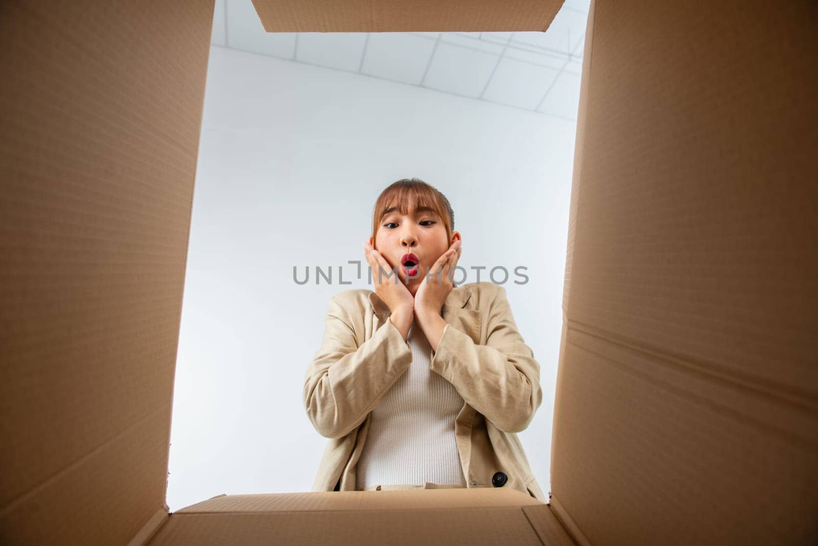 Cheerful Asian young woman opening cardboard box or parcel and looking inside