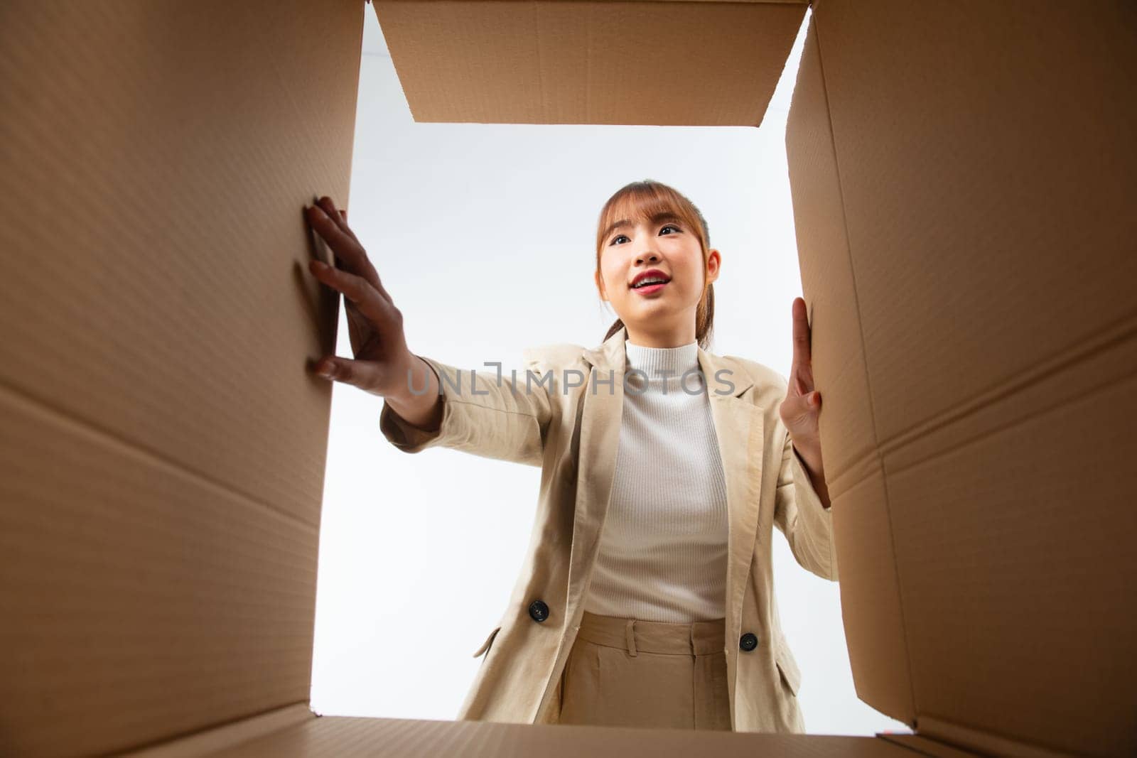 Cheerful Asian young woman opening cardboard box or parcel and looking inside by makidotvn