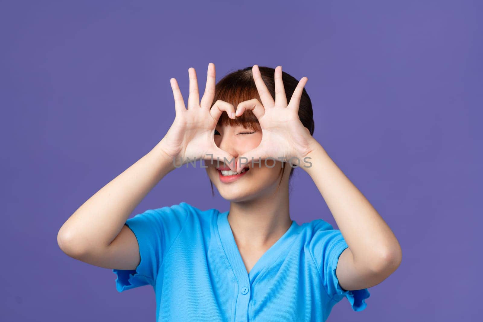 Happy beautiful girl showing heart gesture with fingers isolated over purple background by makidotvn