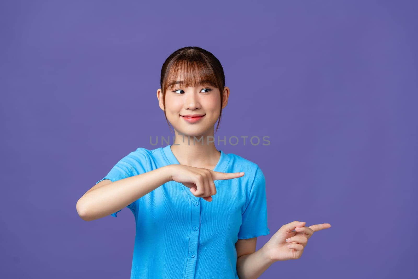 pretty  asian woman smiling happily and pointing to side and upwards with both hands showing object 