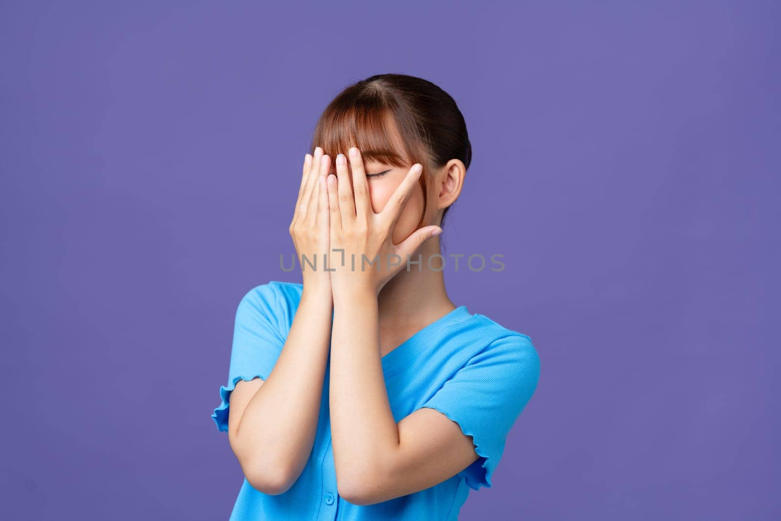 Young woman covering face with hands, looking through fingers, peeking with curiosity at something