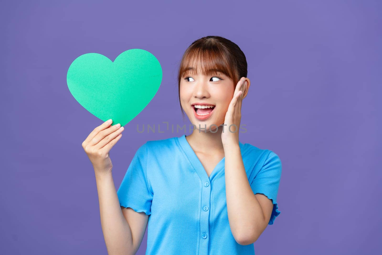 Cheerful young woman hold hands green heart paper shape isolated on purple background