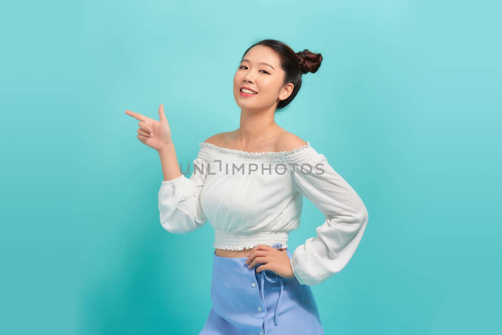Cheerful excited asian woman use finger pointing to side with product over isolated blue background. 