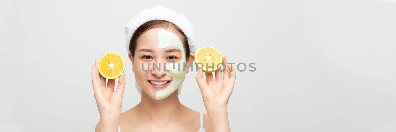 Emotional young woman with facial mask and halves of ripe orange on white background. Web banner.