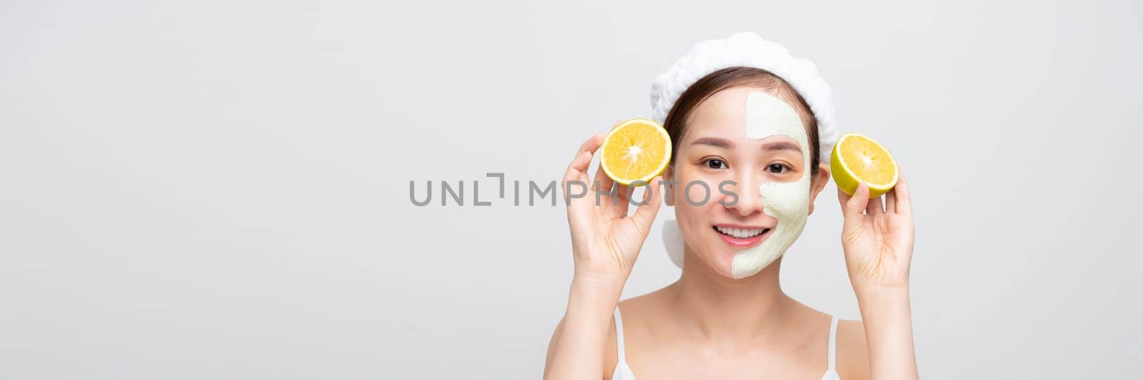 Emotional young woman with facial mask and halves of ripe orange on white background. Web banner.