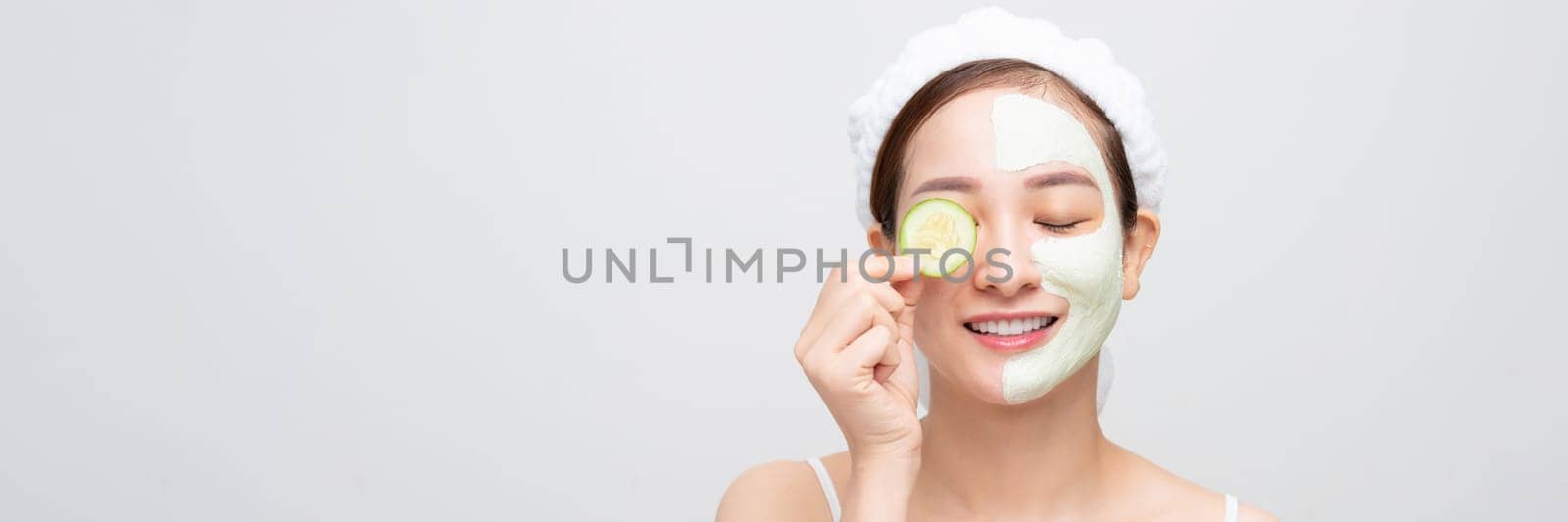 Woman with facial mask holds sliced cucumber, over white banner background