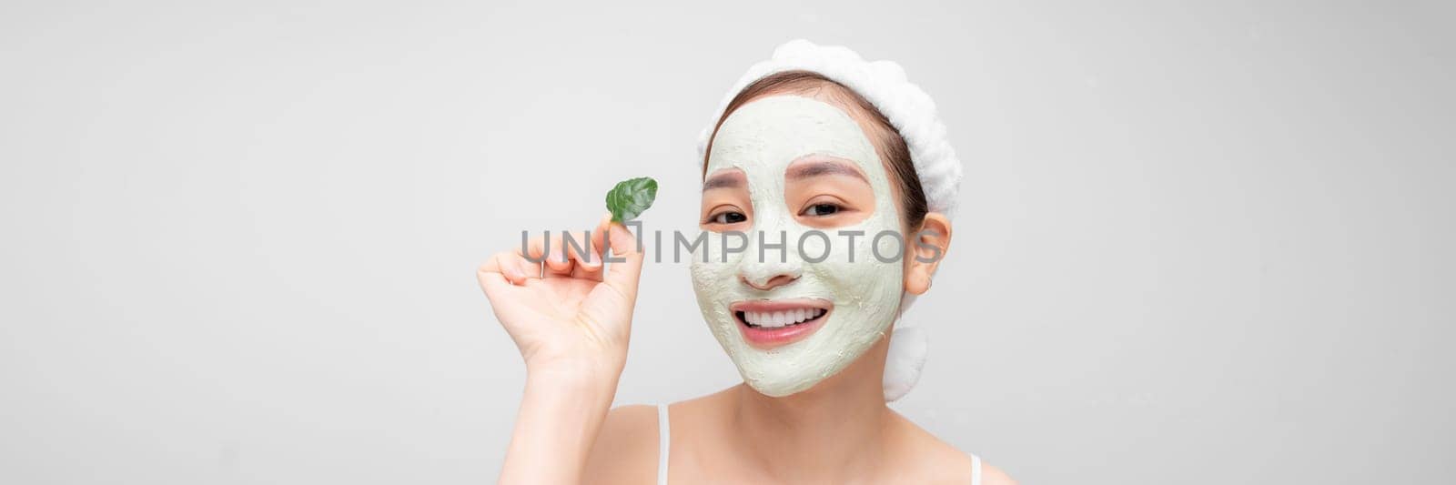 Minimal beauty portrait woman applying white nourishing mask or creme on face, green leaf in hand. banner by makidotvn
