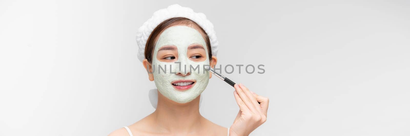 Happy young woman applying a white mask on her face with a brush. by makidotvn