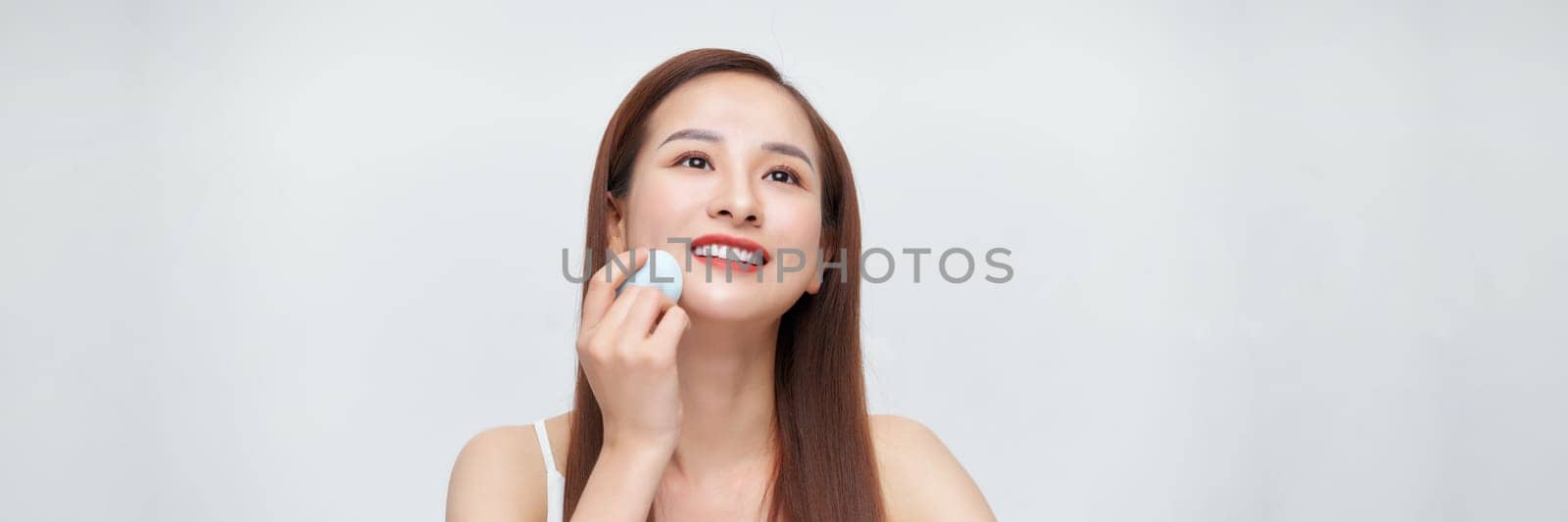 Beautiful happy asian girl using powder sponge isolated over white banner background