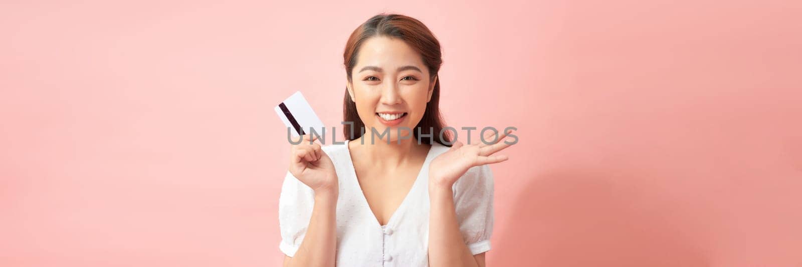 Happy young Asian woman showing credit card with open palm gesture isolated on banner background 