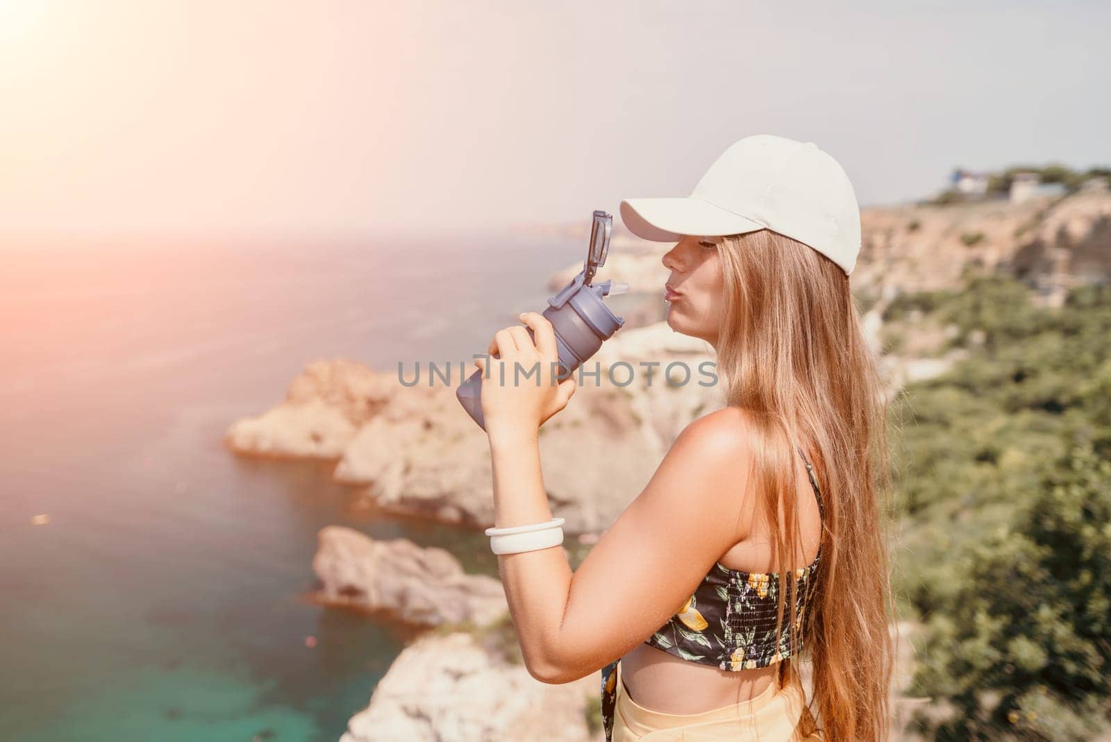 Woman travel sea. Happy tourist drink water on hot summer day. Woman traveler looks at the edge of the cliff on the sea bay of mountains, sharing travel adventure journey by panophotograph