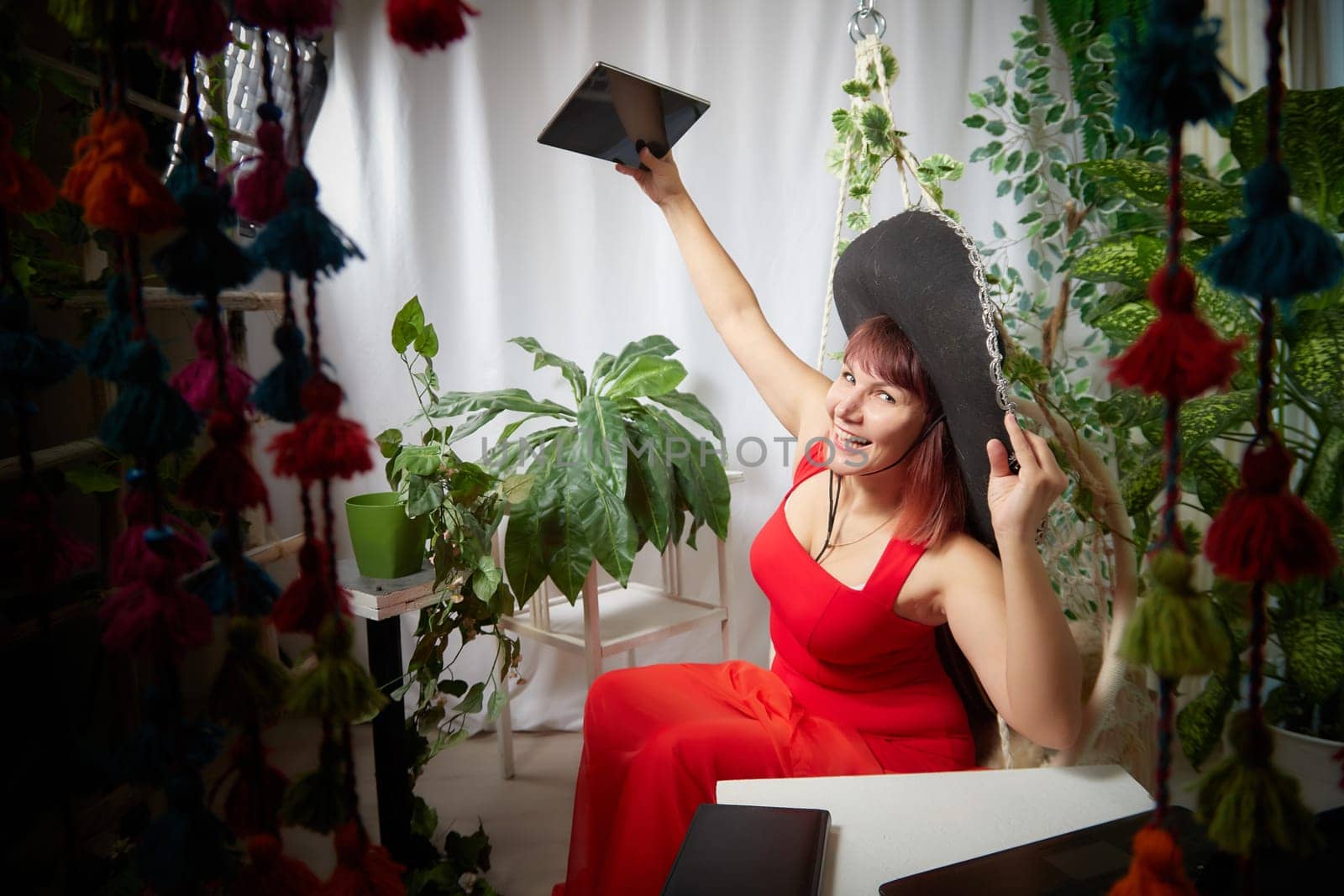 Funny, cute, self-confident adult girl posing in a red dress and taking a selfie. A middle-aged model at a photo shoot in a studio for social networks. Leisure activities by keleny