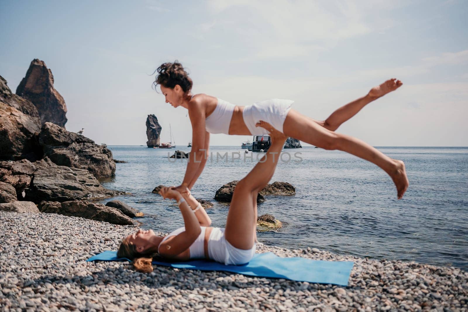 Woman sea yoga. Two Happy women meditating in yoga pose on the beach, ocean and rock mountains. Motivation and inspirational fit and exercising. Healthy lifestyle outdoors in nature, fitness concept. by panophotograph