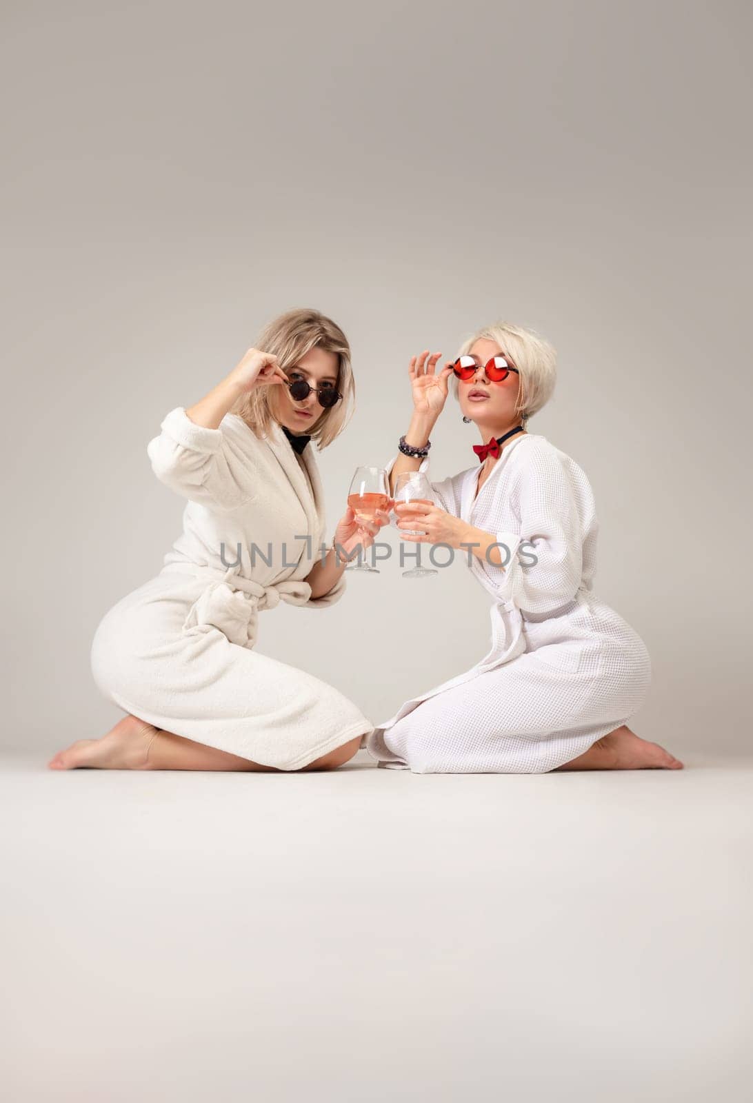 two girls in white coats and glasses with glasses of alcohol are sitting in the studio on a white background of a copy paste