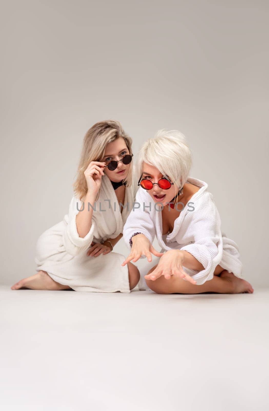 two girls in white coats and glasses are having fun with emotions sitting in the studio on a white background of a copy paste