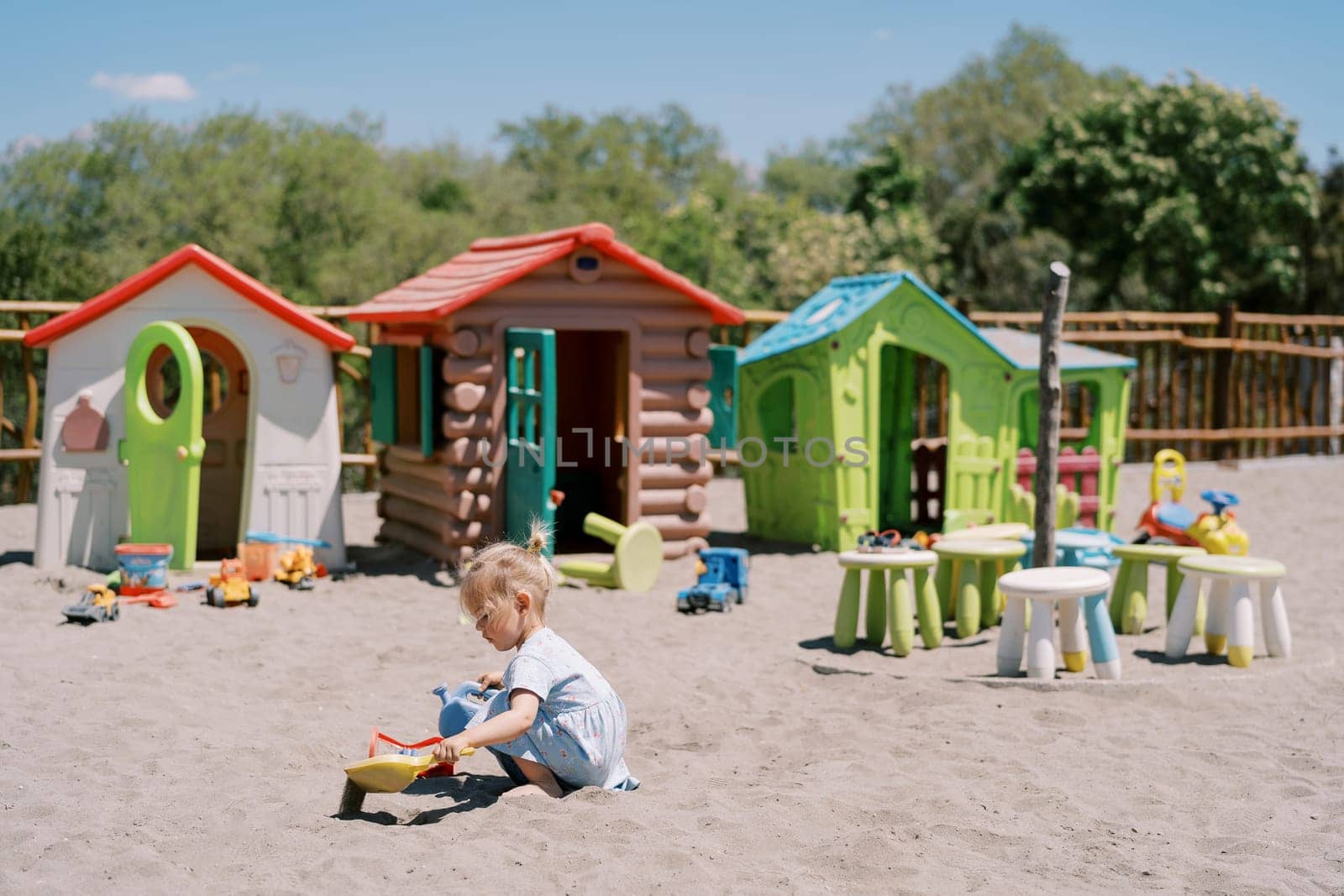 Little girl digs sand with a shovel on the playground near toy houses. High quality photo