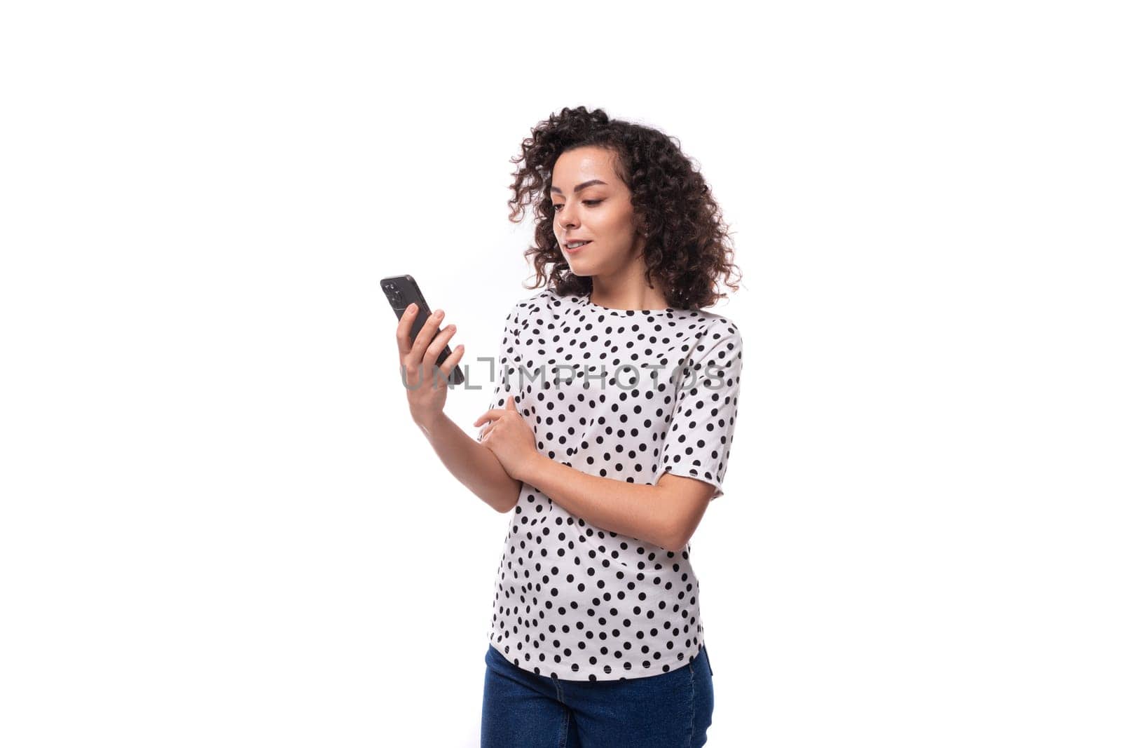 young confident well-groomed brunette curly woman dressed in a blouse with a pattern of peas reads a message on the phone.